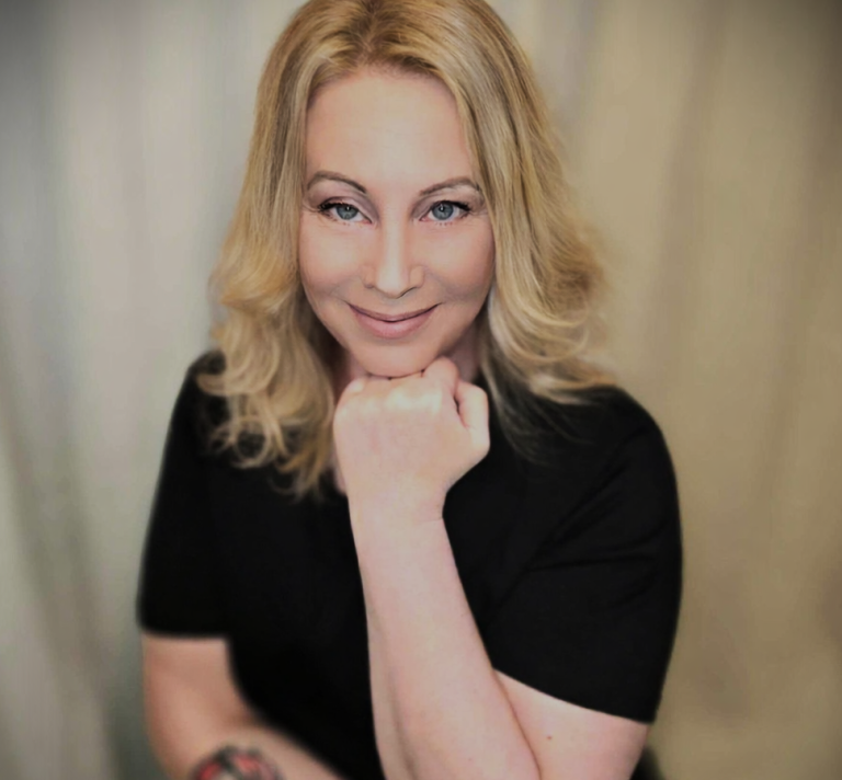 En blond kvinna tittar in i kameran och ler