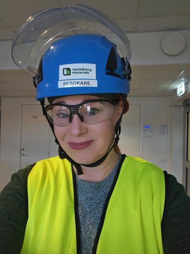 Kvinna med säkerhetsutrustning, hjälm och skyddsglasögon, bär en gul väst.